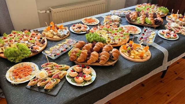 Stół z cateringiem: croissanty, tartaletki, śledzie, deska serów i koreczki