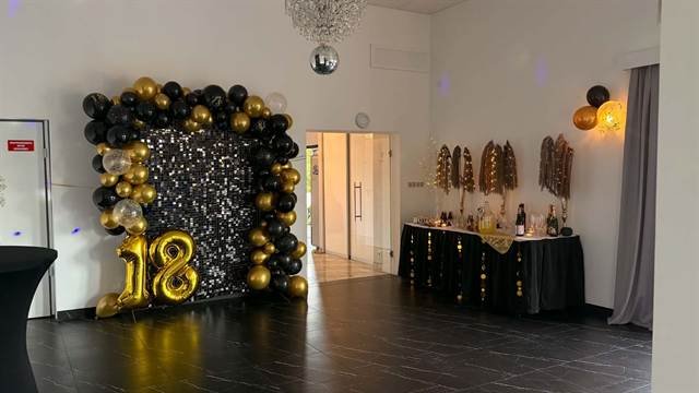 Ścianka z czarnych i złotych balonów z cyfrą 18 oraz stół z napojami